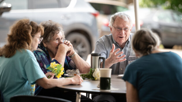 A small group of First U folks chat and share a meal together under the tent.